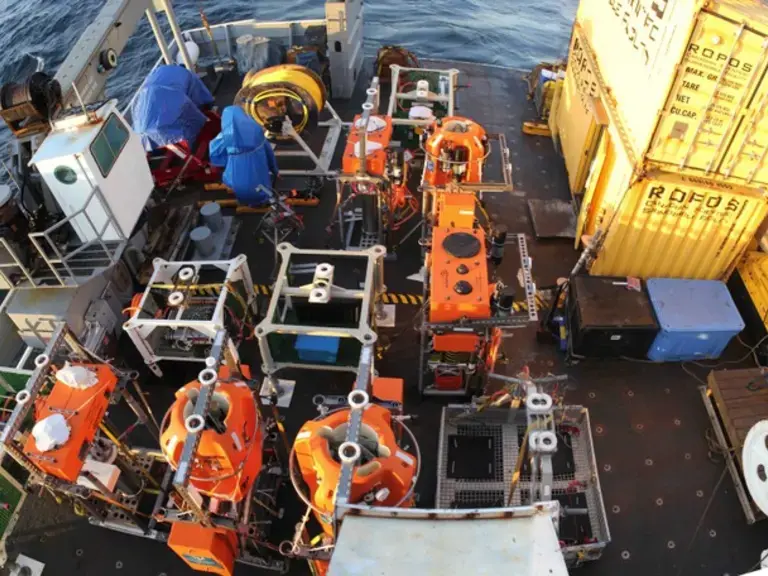 A ship deck crowded with orange oceanographic equipment